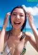 A woman in a bikini on the beach laughing.