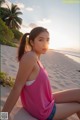 A woman in a pink tank top sitting on a beach.