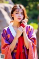 A woman in a purple and red kimono holding a red rose.