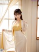 A woman in a yellow and white dress standing by a window.