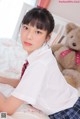 A woman in a school uniform sitting on a bed with a teddy bear.