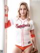 A woman in a baseball uniform leaning against a wall.