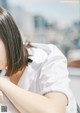 A woman in a white shirt leaning against a wall.