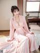 A woman in a pink robe sitting on a bed.